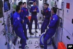 In this photo released by Xinhua News Agency, an image captured off a screen at the Jiuquan Satellite Launch Center in northwest China shows the Shenzhou-15 and Shenzhou-14 crew chatting after a historic gathering in space, Nov. 30, 2022.