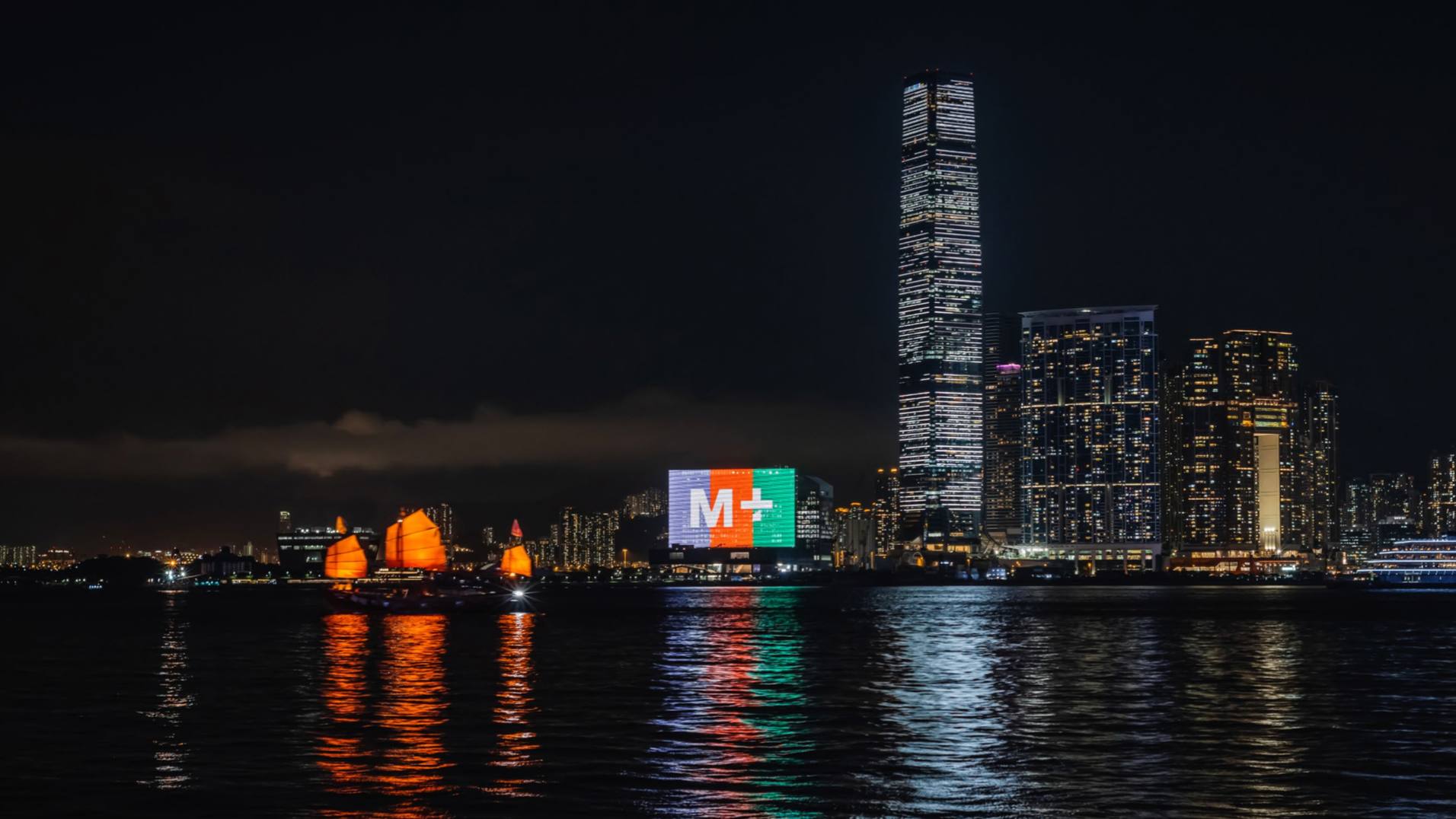 The new gallery at night lit up against a backdrop of Hong Kong skyscrapers