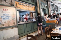FILE - A cook gives a customer a souvlaki, a popular Greek fast food made with pieces of meat grilled on a skewer, in a restaurant, in Athens, May 27, 2022.