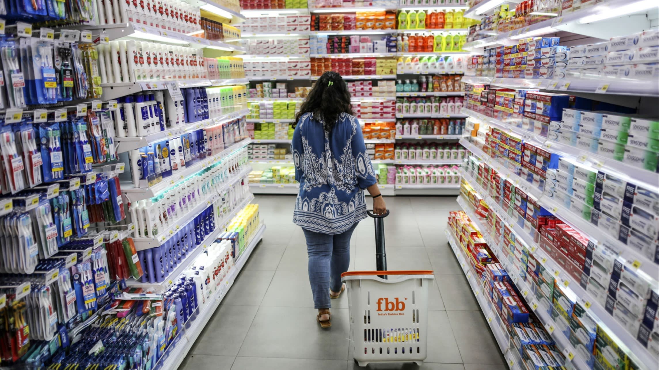 A shopper drags a basket through an aisle of personal care goods at a hypermarket in Mumbai