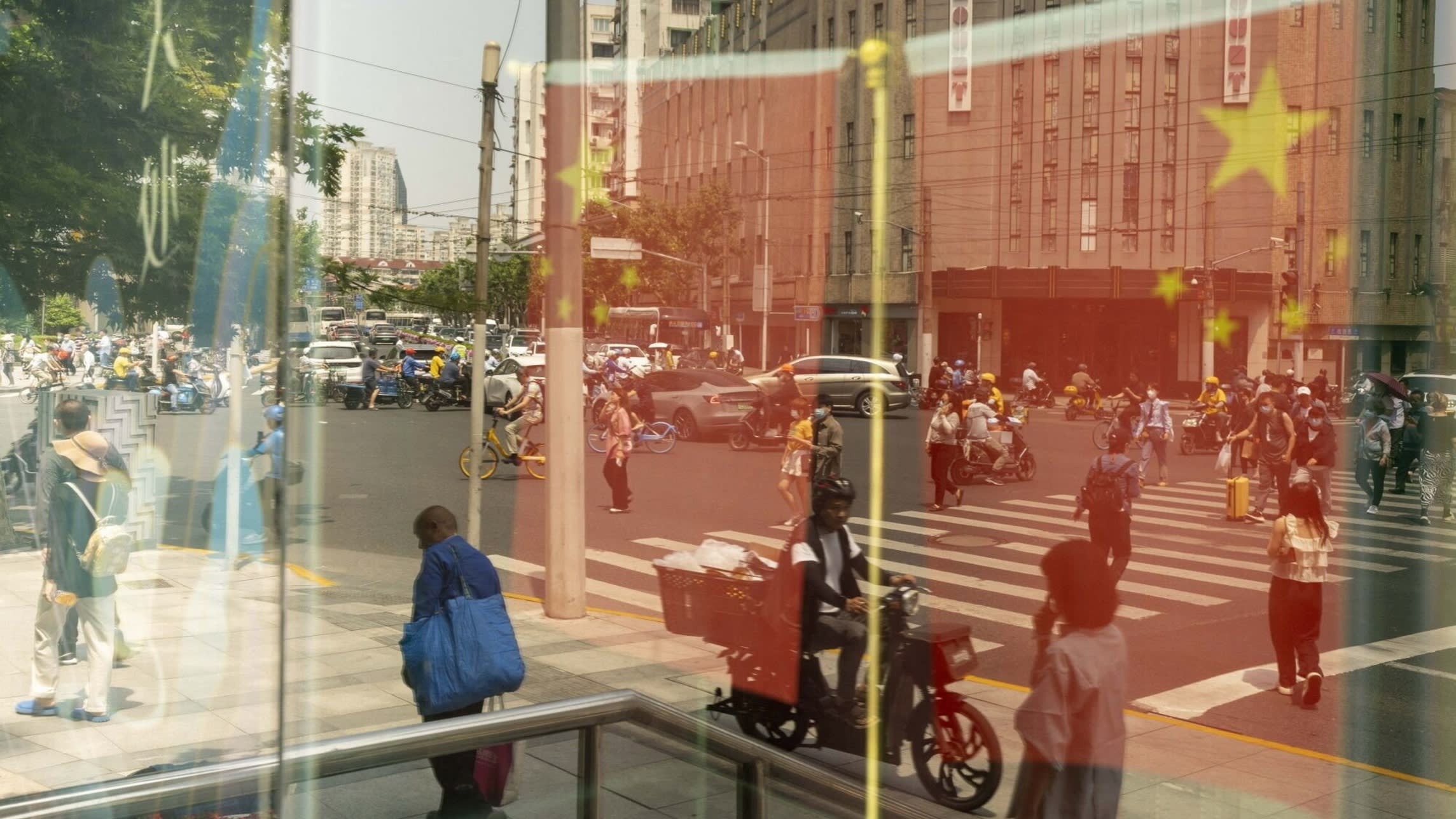 Chinese flags and pedestrians reflected in a window in Shanghai