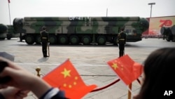 FILE - Onlookers wave Chinese flags as military vehicles carrying DF-41 ballistic missiles roll during a parade in Beijing, China, Oct. 1, 2019.