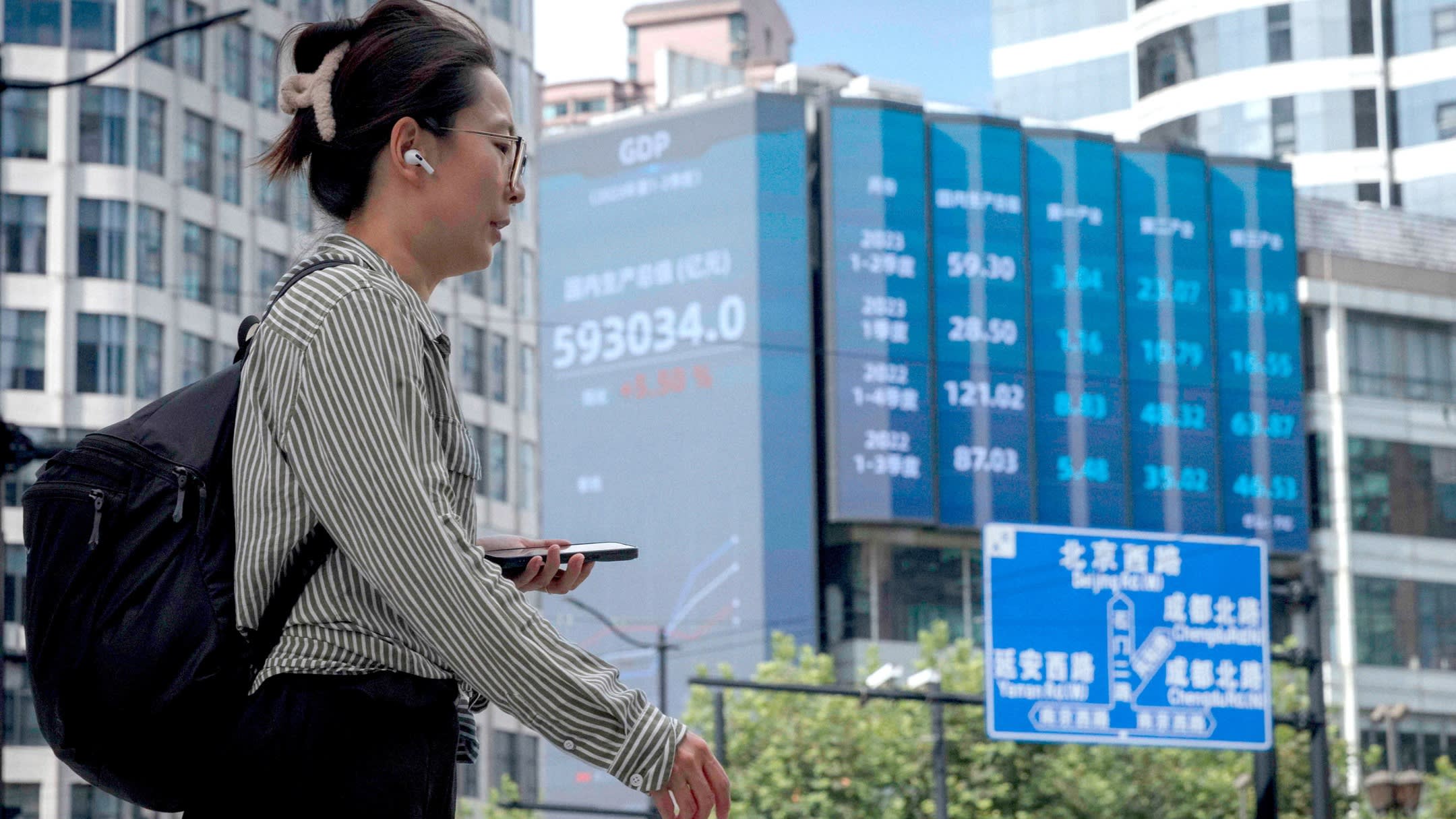 A woman walks past a screen showing stock exchange data in Shanghai, China