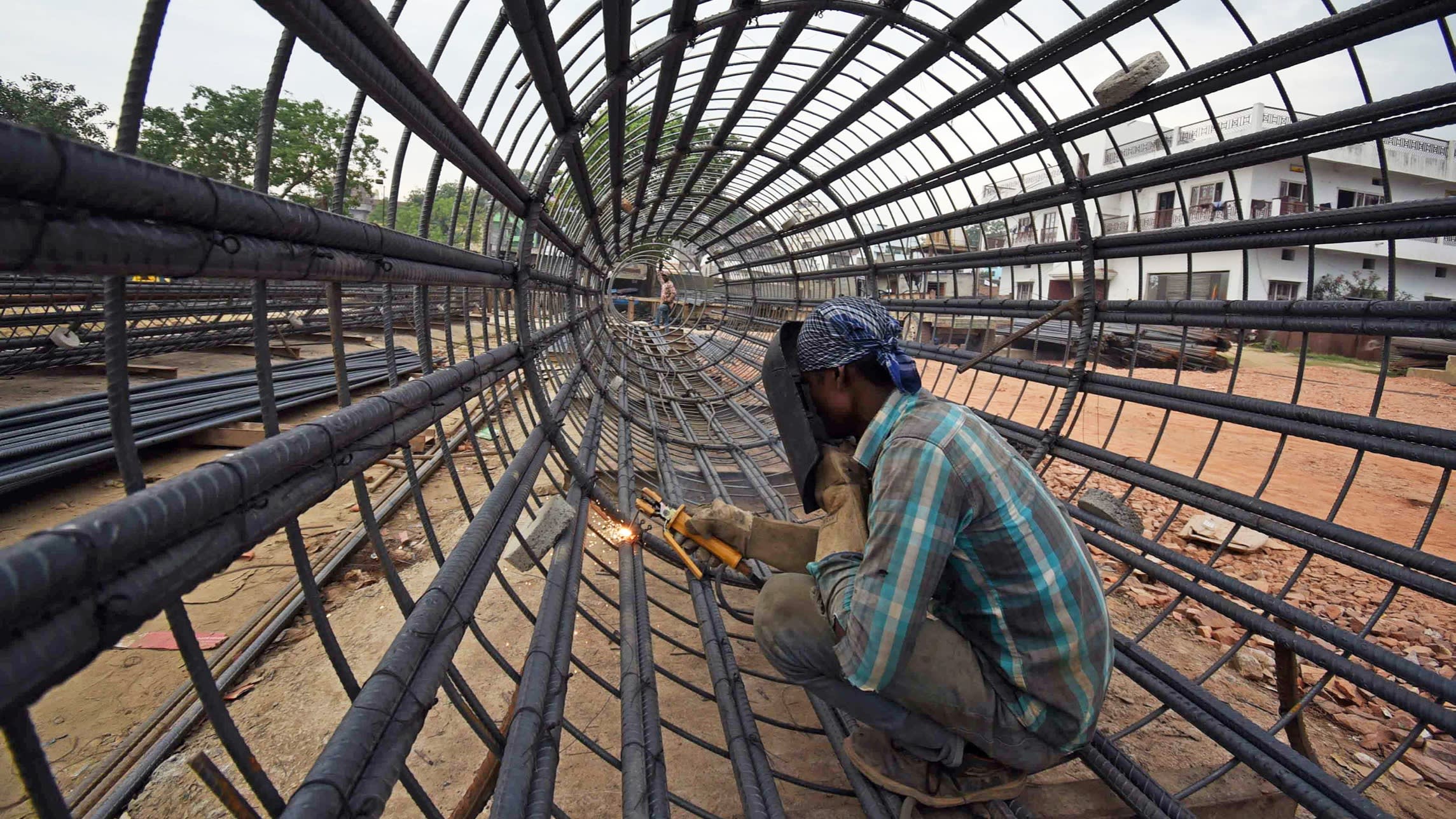 A man with a visor welds a joint on a cylindrical metal frame