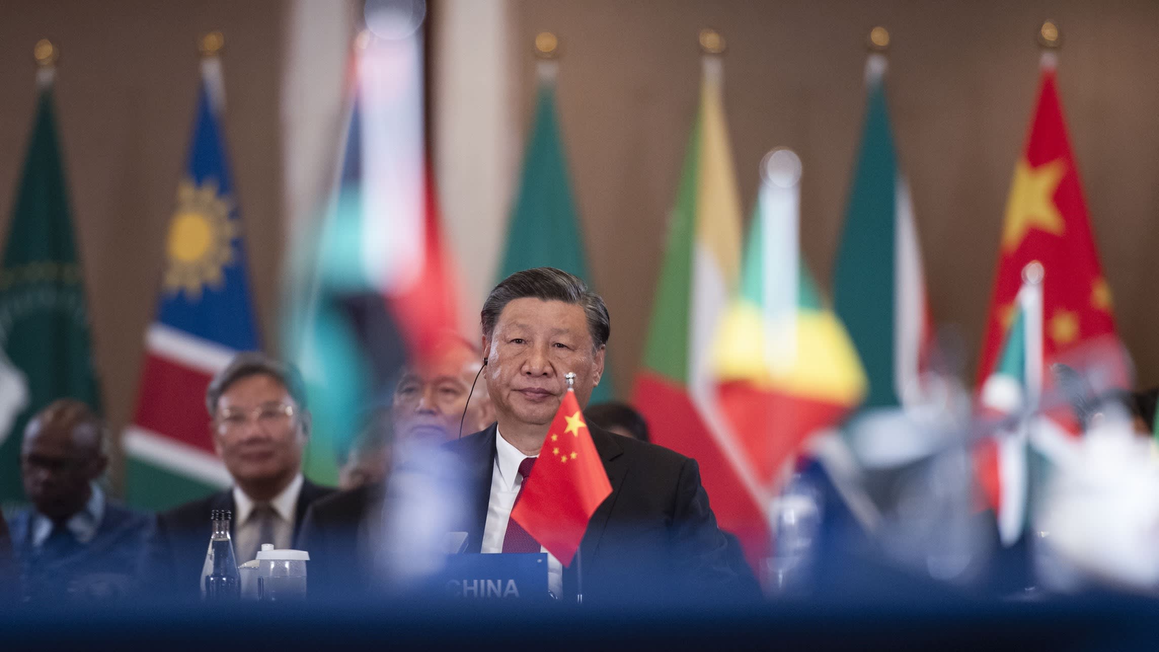 Xi Jinping wearing an earpiece with the flag of China on the table in front of him