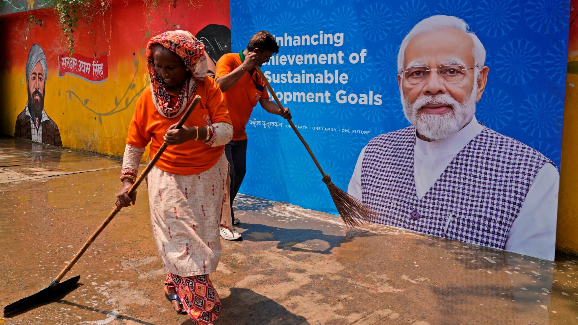Municipal workers clean a sidewalk near a billboard featuring Indian prime minister Narendra Modi in New Delhi