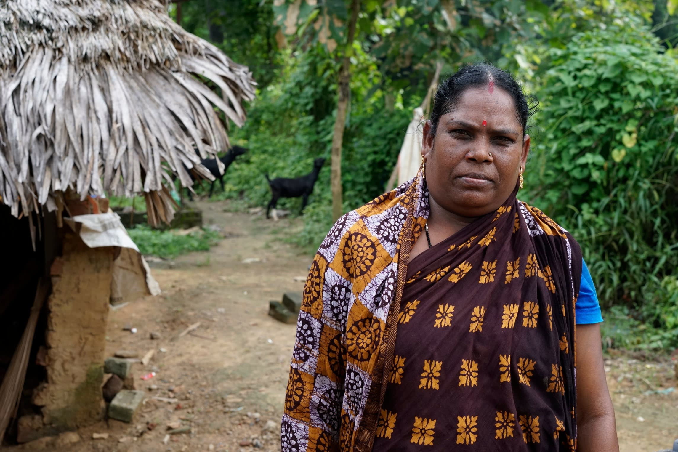 An Indian woman stands beside a basic shack
