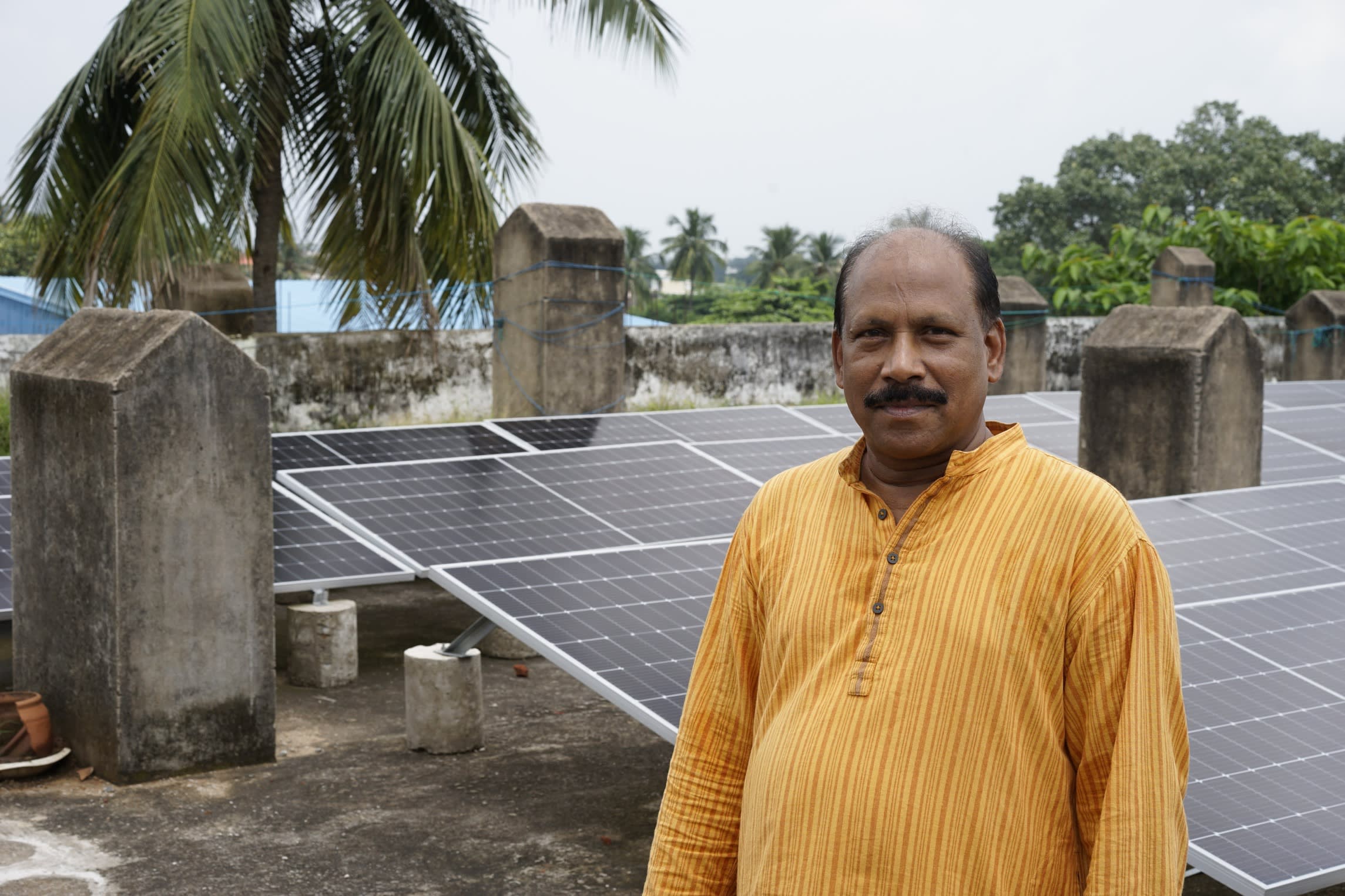 An Indian man stands in front of solar panels mounted on a roof
