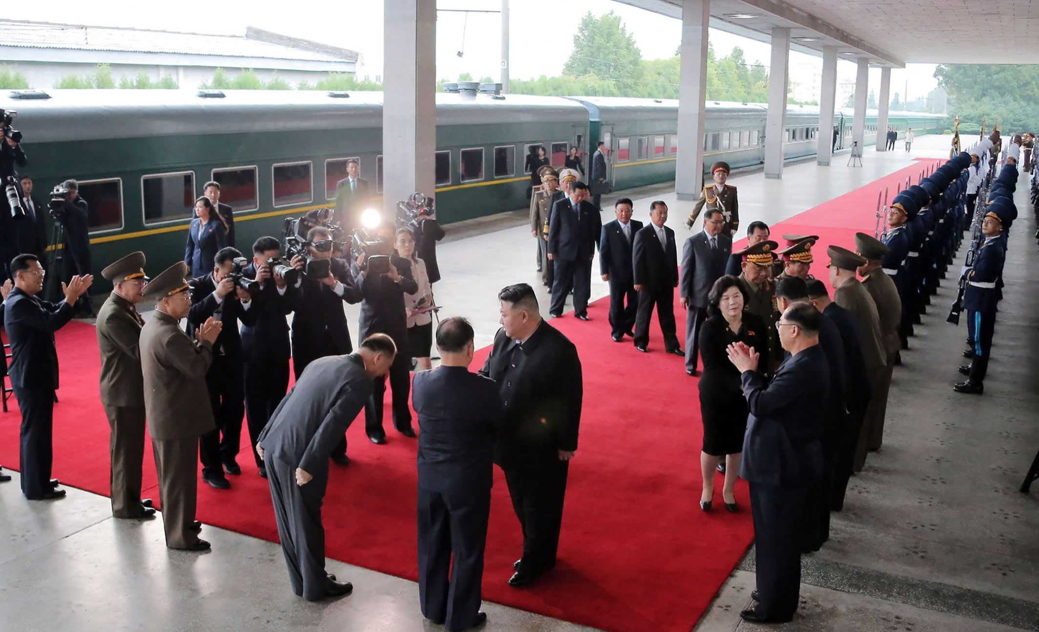 Kim on a red carpet at a railway station with bowing and applauding officials and generals