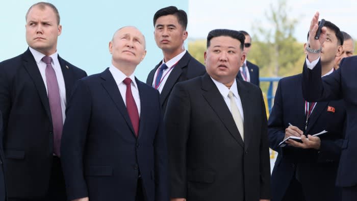 Men in suits stand in a launch site of a rocket