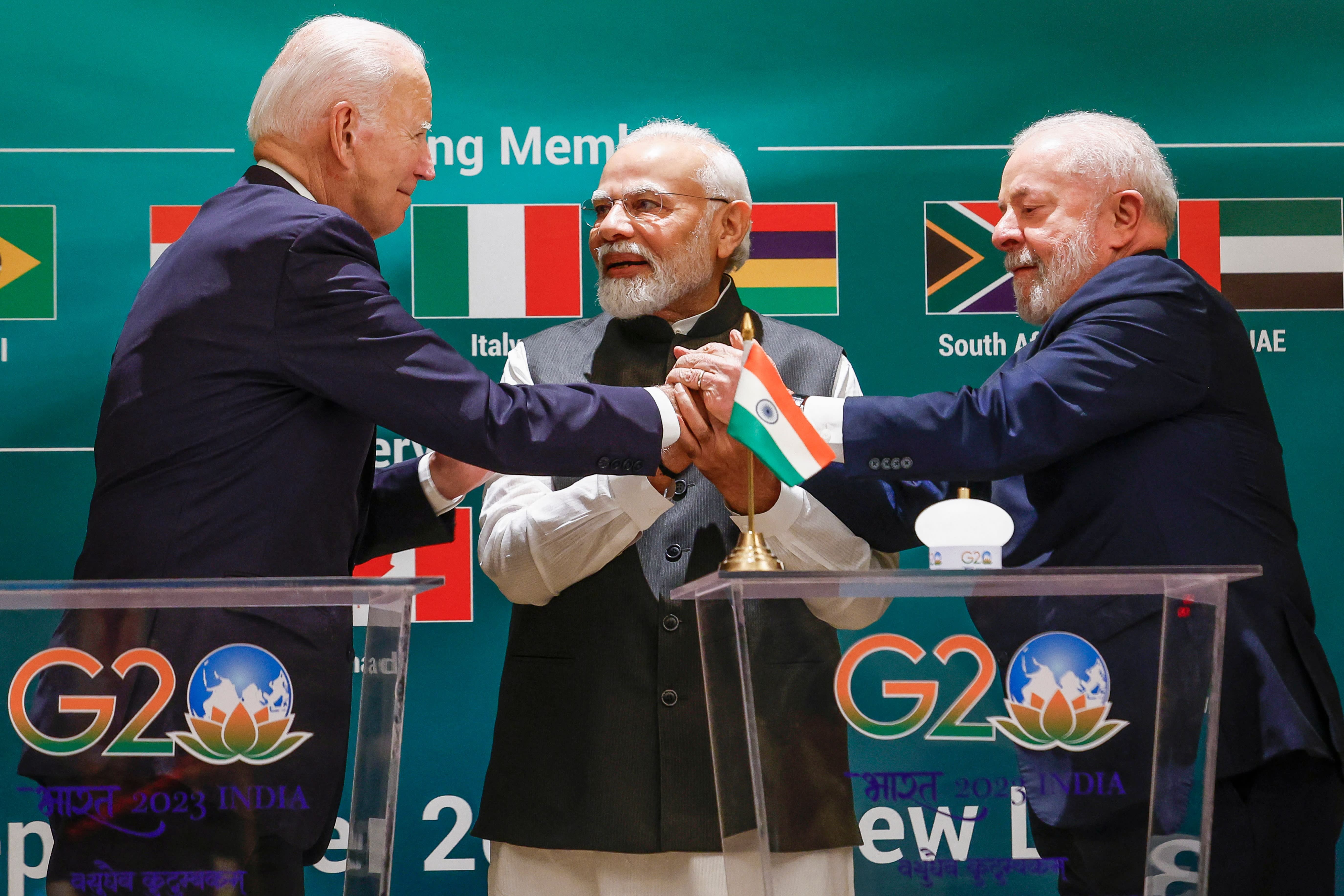 Three men clasping hands on stage at the G20