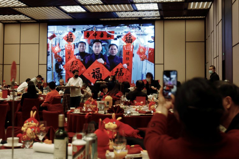 ENG_CHN_NewYearsEve_10262023.3.JPG A woman takes pictures of a screen displaying Spring Festival greetings from Chinese astronauts Fei Junlong, Deng Qingming and Zhang Lu aboard China's space station, during a Lunar New Year's Eve dinner service at Shangri-La Shougang Park hotel in Beijing, Jan. 21, 2023. Credit: Florence Lo/Reuters