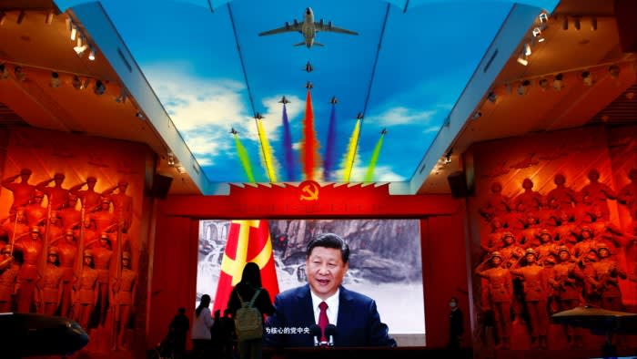 Visitors stand in front of a giant screen displaying President Xi Jinping next to a flag of the Chinese Communist party at a military museum in Beijing