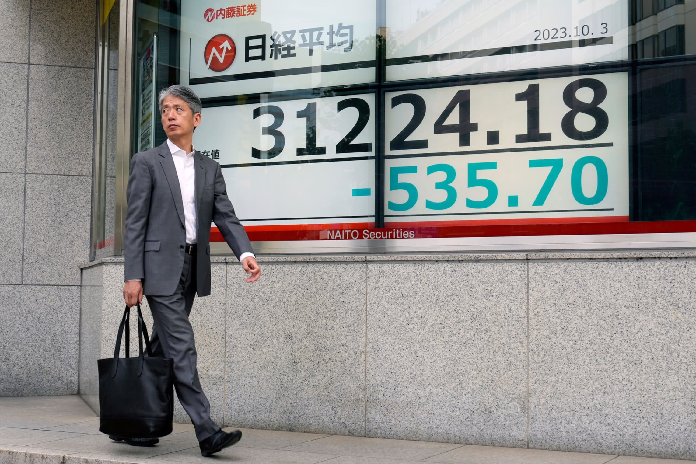 A passer-by walks past a stock market indicator board in Tokyo