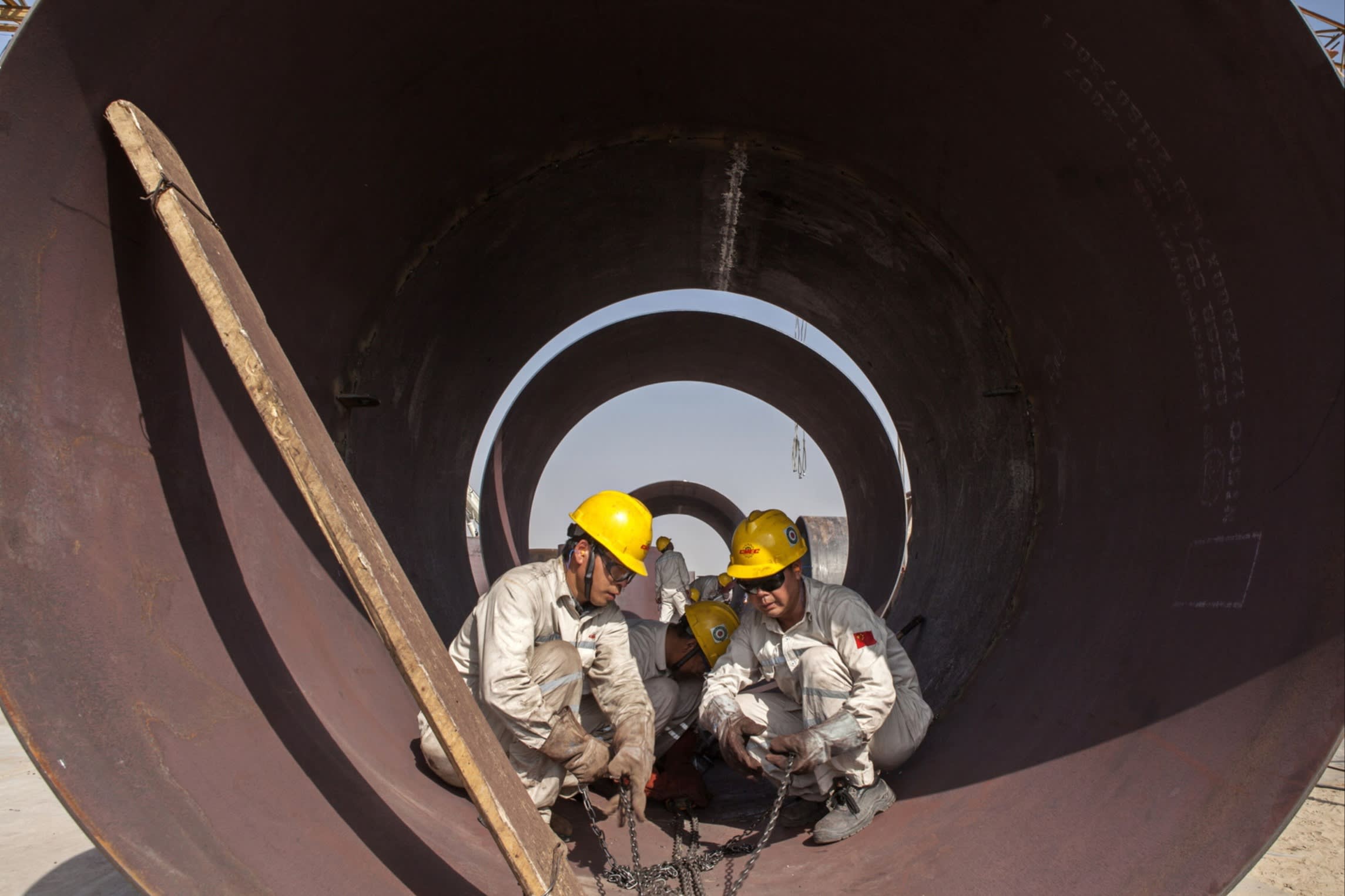 Construction workers stand inside a huge metal pipe