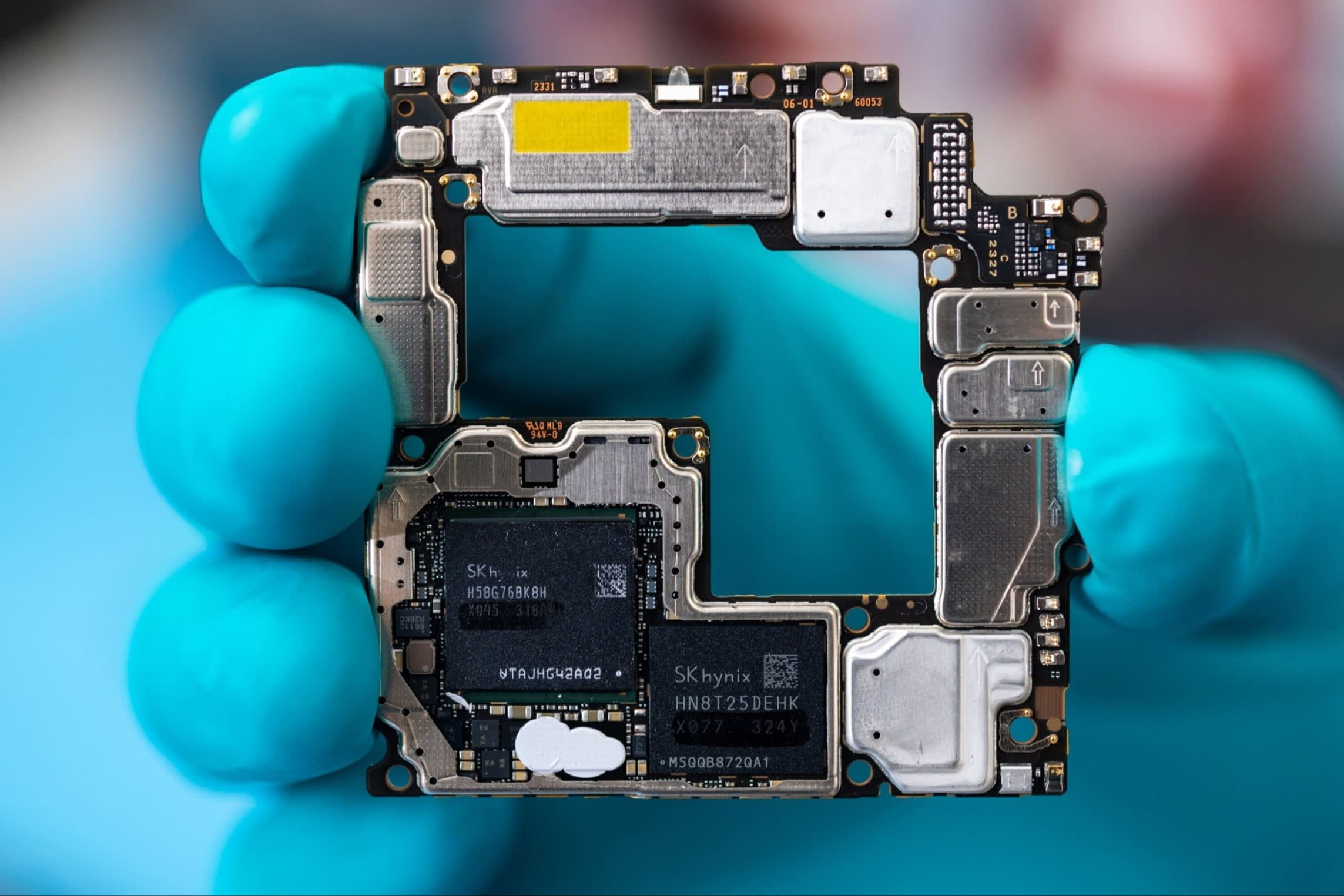 A hand in a turquoise latex glove holds the working components of the Mate X5 smartphone