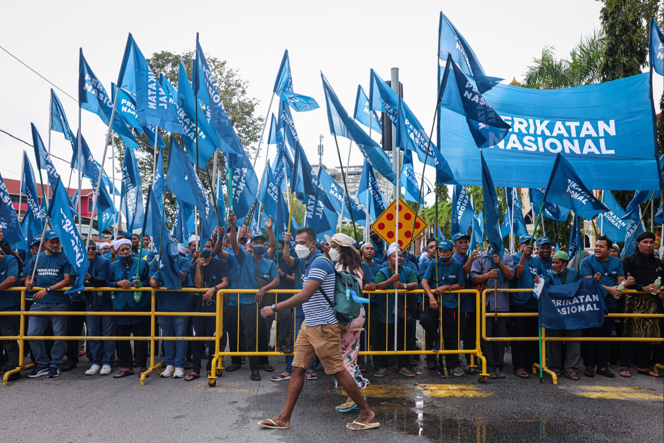 Tourists walk pass ‘Perikatan Nasional’ (National Alliance) coalition supporters 