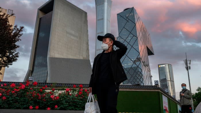 A man wears a protective mask as he walks by the skyline of Beijing’s central business district