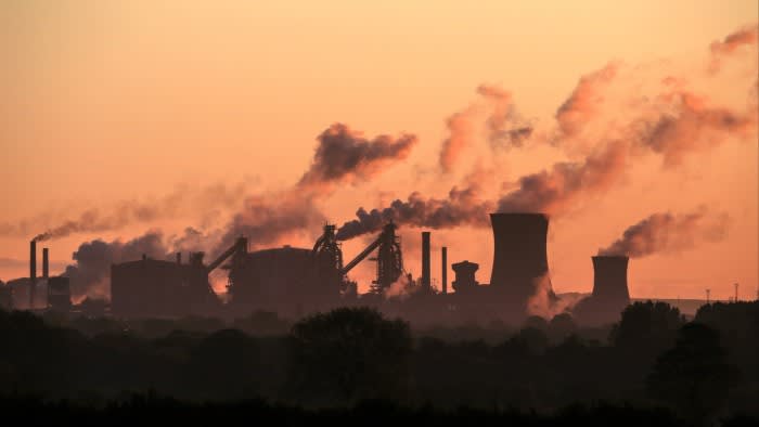Steel plant with smoking chimneys silhouetted against a sunset