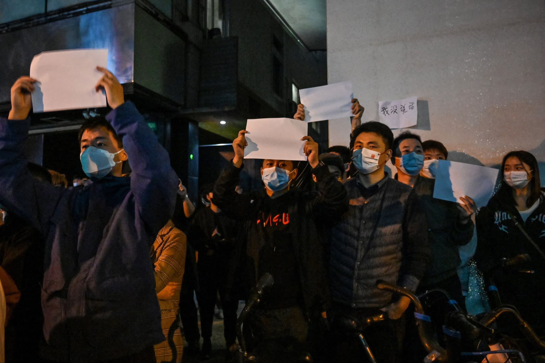 People hold up blank sheets of paper in a street protest