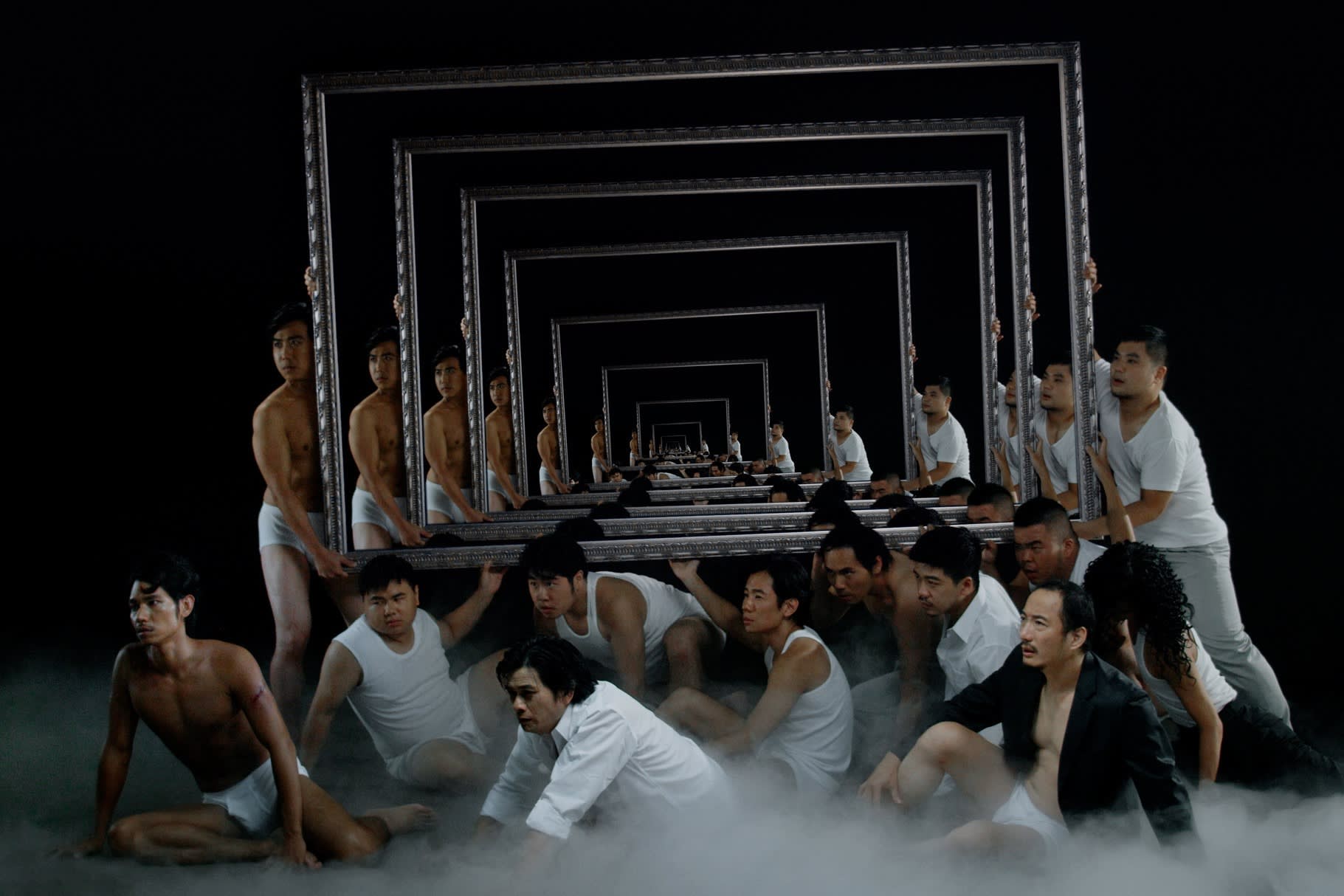 A film still showing a group of men crouching on a fog-covered ground, holding a mirror which shows their repeated reflections.