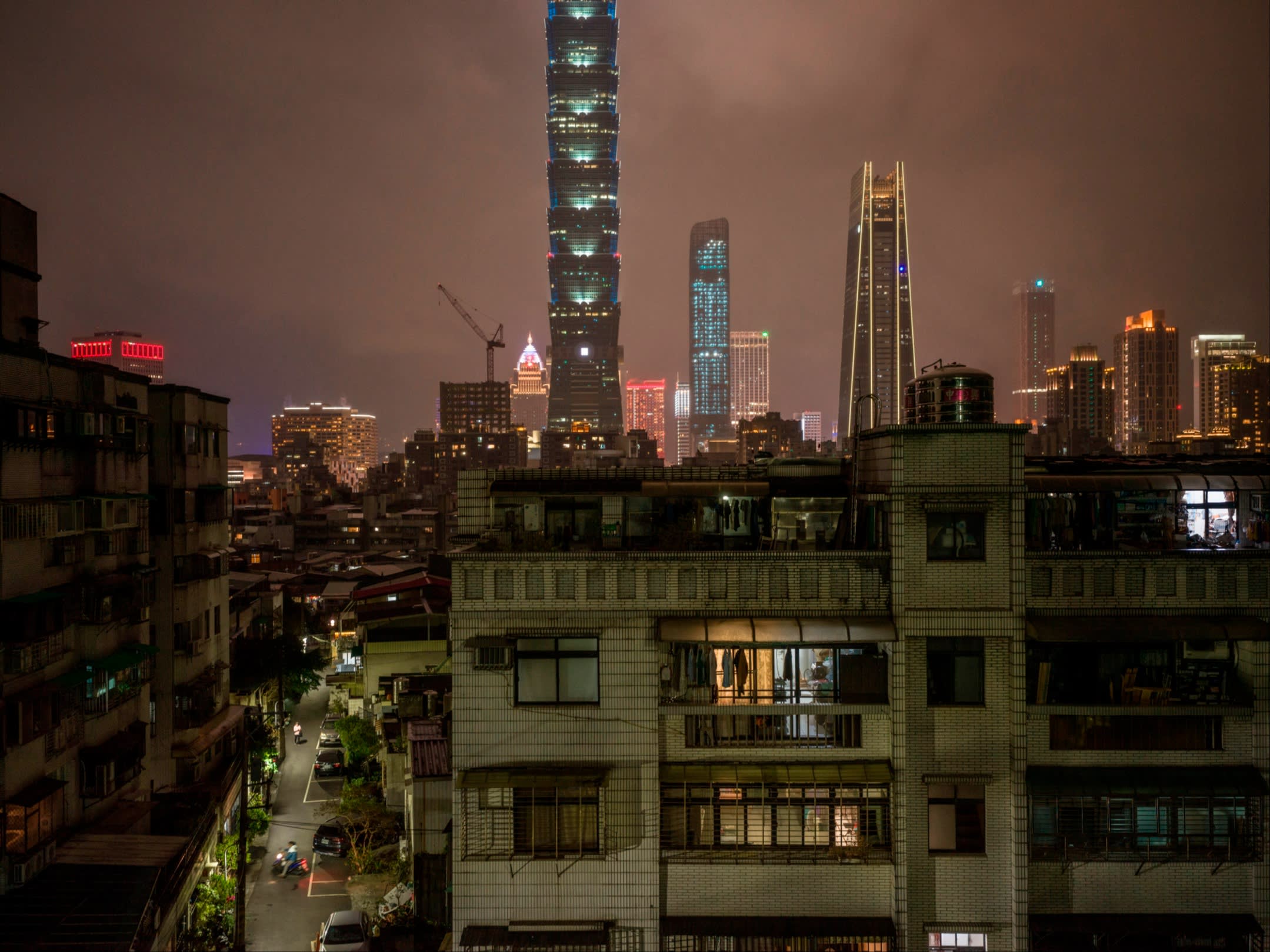 The windows of apartment blocks lit up against a backdrop of skyscrapers in Taipei at night