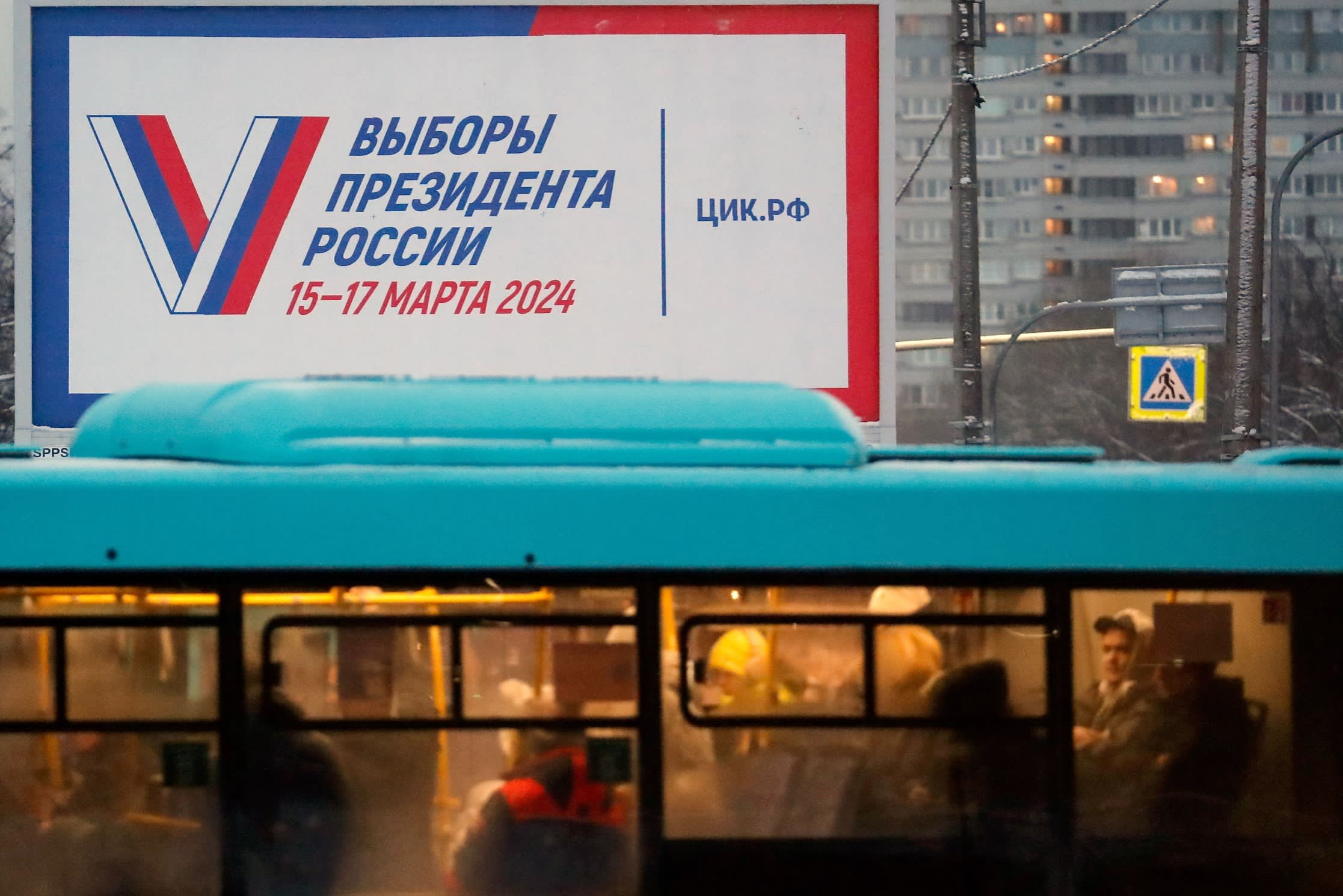 People ride on a bus past a billboard announcing the 2024 presidential election in St Petersburg, Russia,