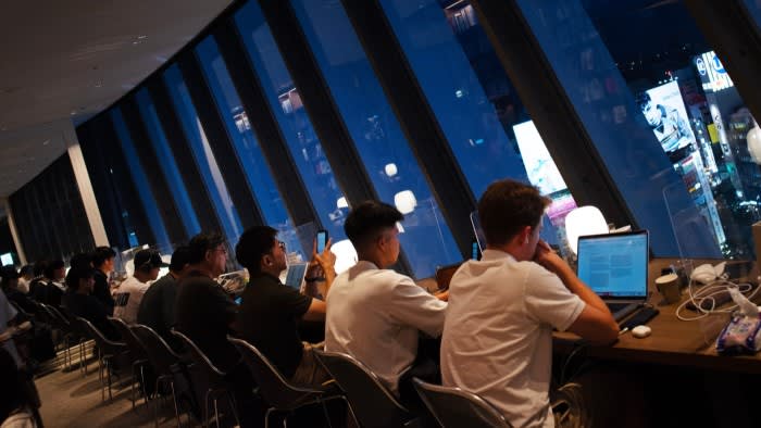 A row of customers sitting at a long desk in front of laptops at Tsutaya Share Lounge, by a window high above central Tokyo