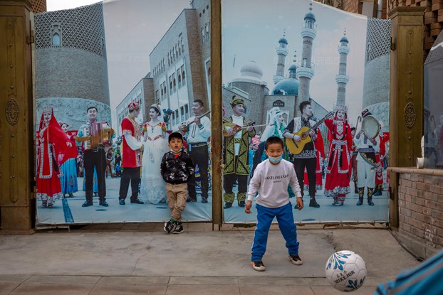 ENG_UYG_BlendEthnicities_01192024_02.jpg Children play soccer in front of a gate with a mural depicting Uyghur musicians in Urumqi, capital of northwest China's Xinjiang region, April 21, 2021, during a government organized trip for foreign journalists. (Mark Schiefelbein/AP)