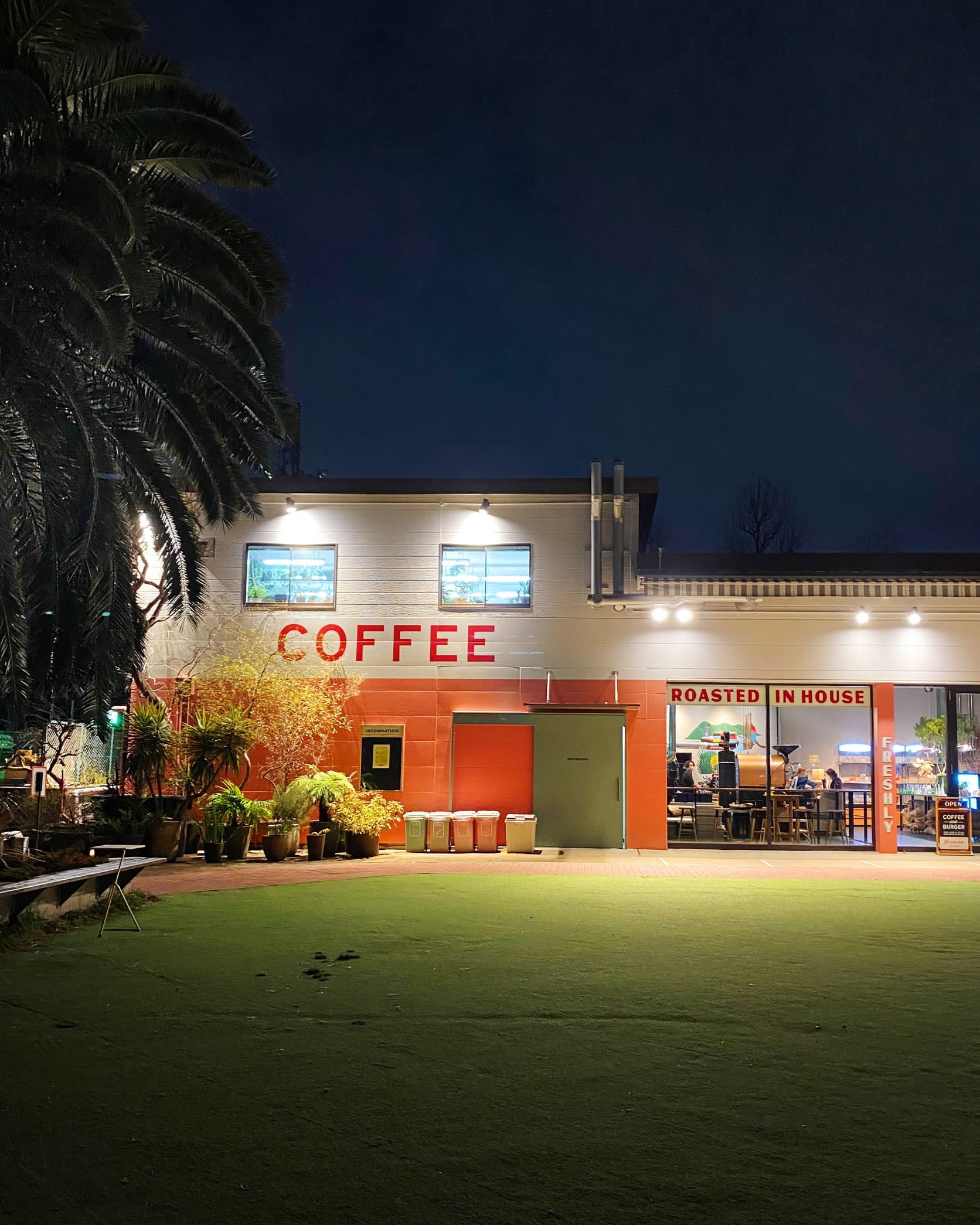 The red and white facade of Little Darling Coffee Roasters photographed in the evening. Its artificial lawn is in the foreground