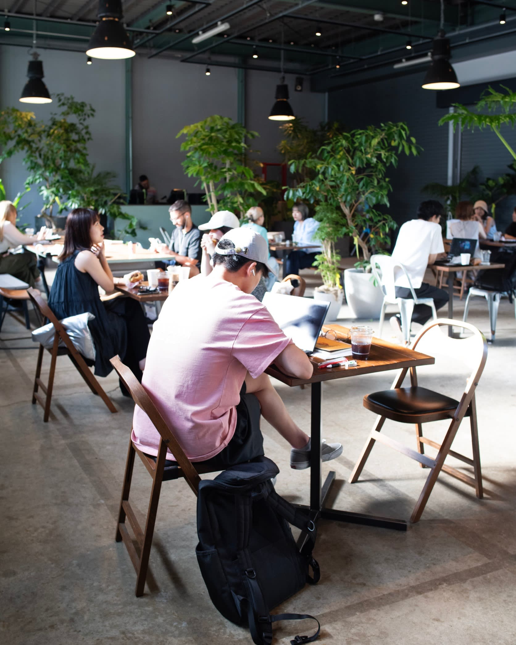 Customers working at individual tables at Little Darling Coffee Roasters, with lots of greenery in the background