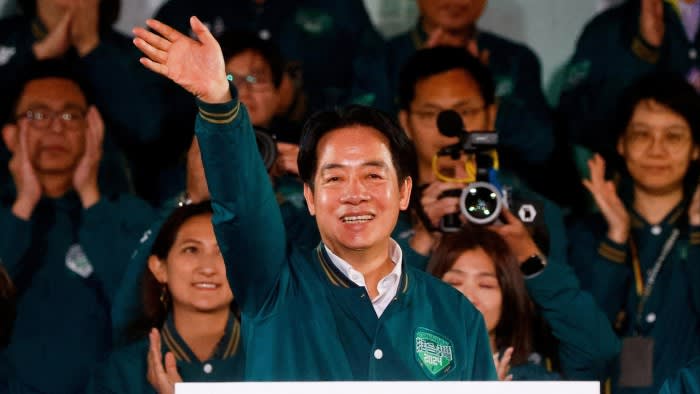 An Asian man waves to a crowd and is flanked by supporters