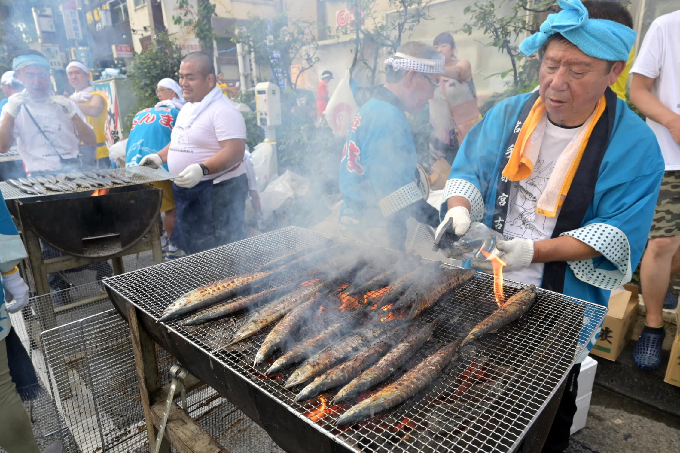 A man in a blue gown and headband grilling saury at the Meguro Citizens’ Festival