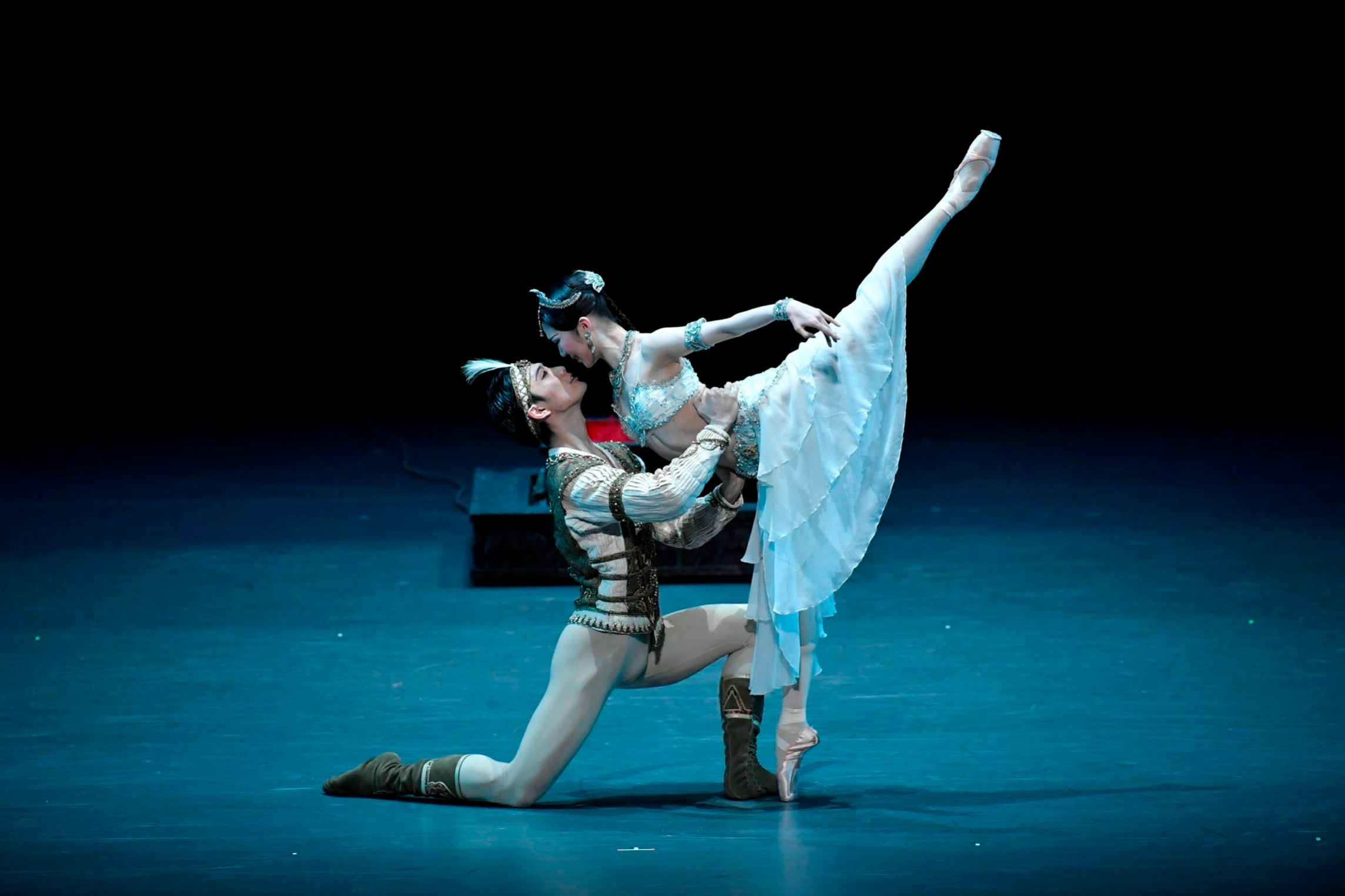 The National Ballet of Japan’s production of ‘La Bayadère’, with a male and female dancer holding each other on a blue-lit stage