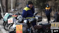 FILE - A migrant worker stands next to signs advertising his work skills on a street as he waits to get hired in Shenyang, in northeastern China's Liaoning province on Feb. 25, 2021
