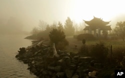 FILE - A woman walks her dog through morning fog near the Fuzhou Ting Pavilion at the Chinese Reconciliation Park in Tacoma, Wash., on Dec. 7, 2017. The pavilion was donated by officials in Fuzhou, China, one of Tacoma's sister cities.
