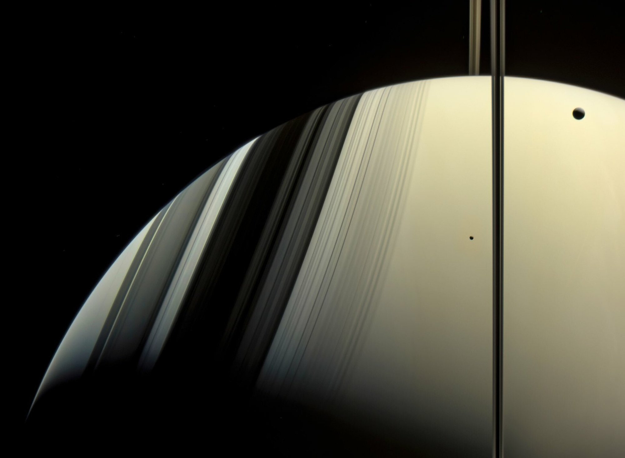 Minas appears as a small dot above Saturn, to the left of the vertical ring shadow. Tethys, a larger Saturnian moon, can be seen in the top right corner. Image: Nasa