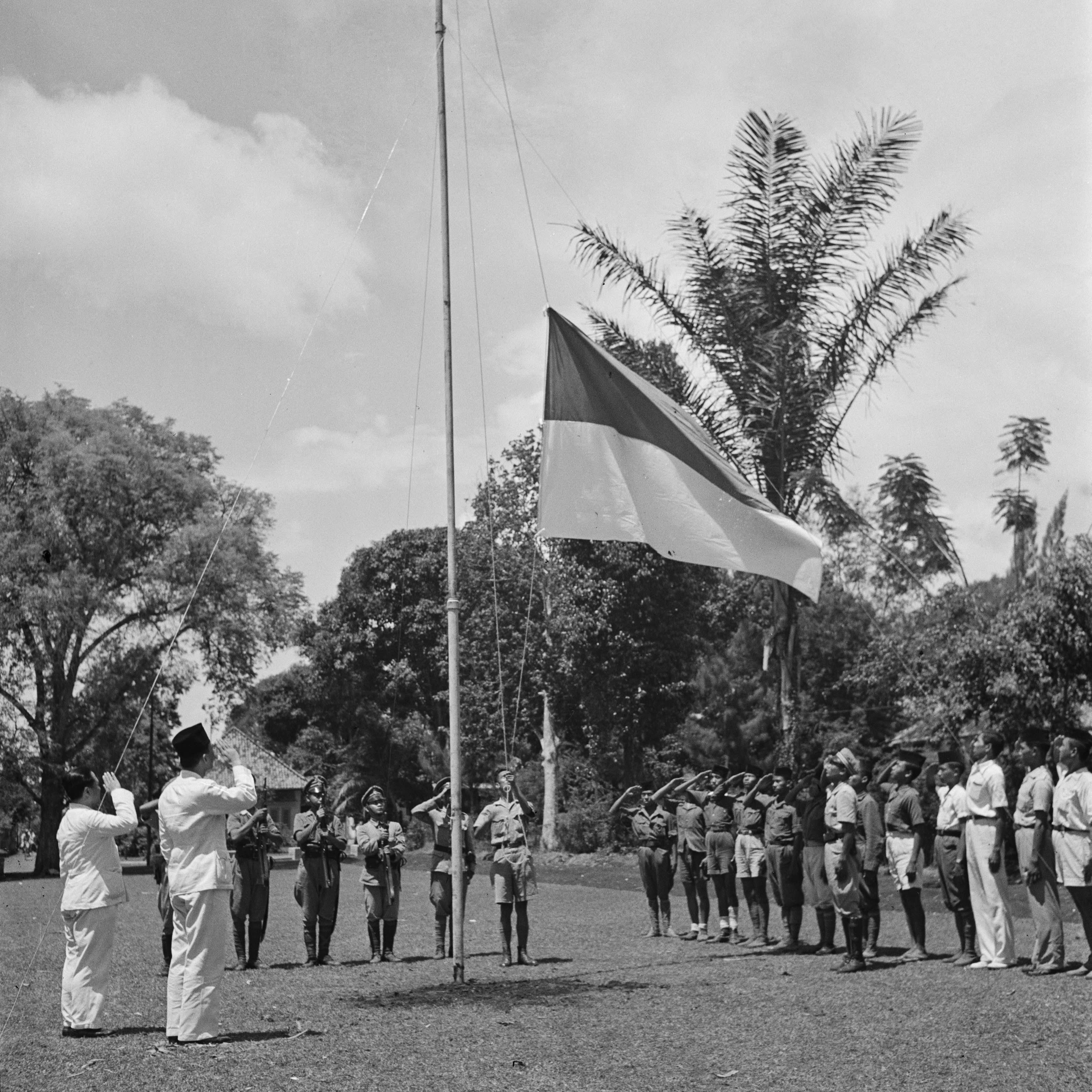 Sukarno and another figure in uniform salute as a flag is raised