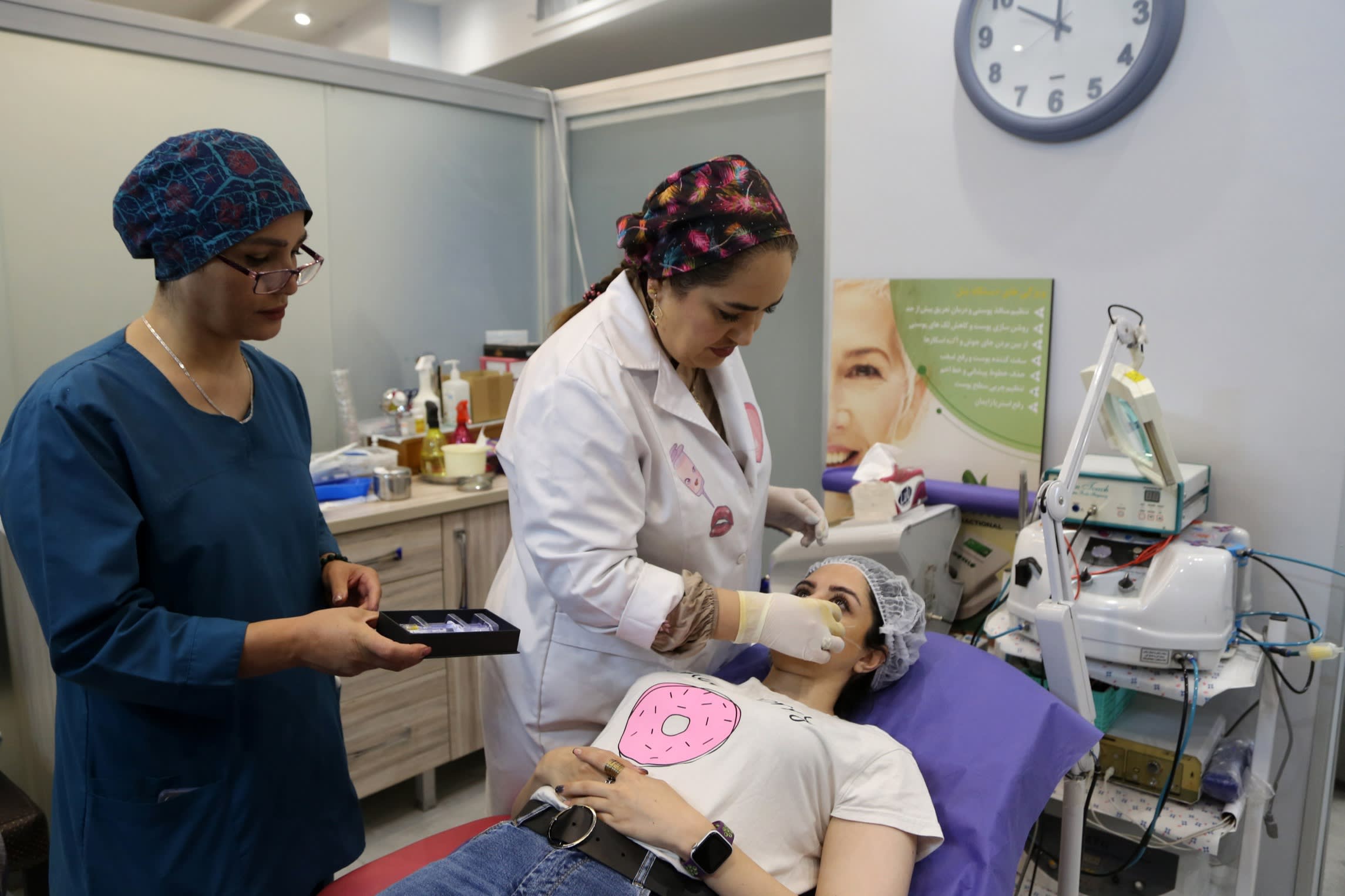 Two clinic employees stand over a patient lying down in a cosmetic surgery clinic