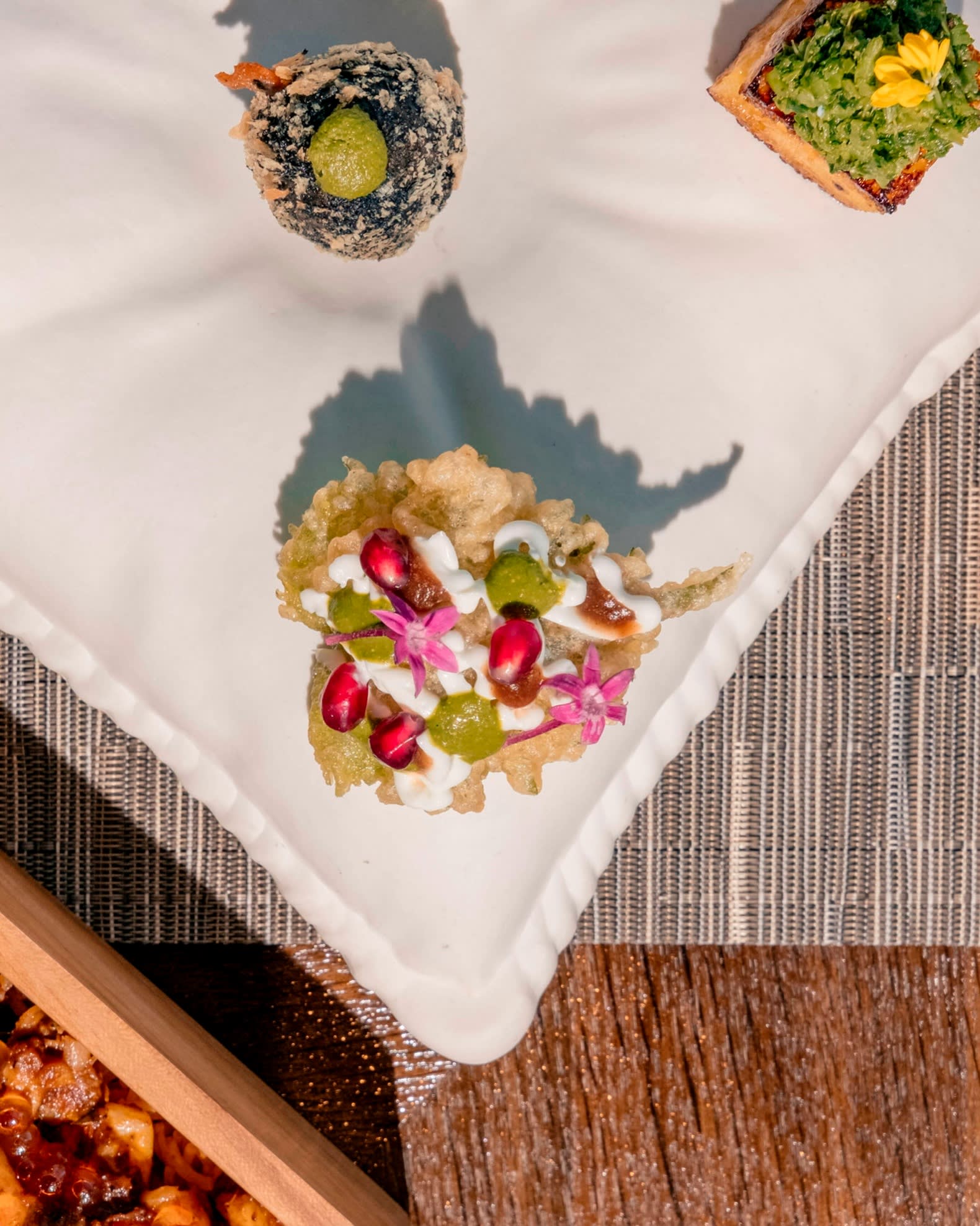 Three of Spice Lab Tokyo’s selection of bites inspired by street foods from India, including dhokla (steamed chickpea cake) and shiso-leaf chaat, positioned on a cushion and photographed from above