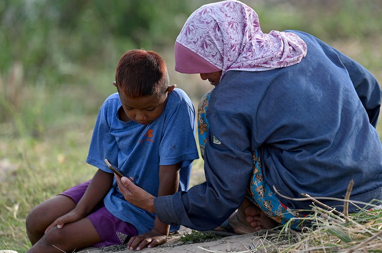 ENG_WOMEN'S_Analysis_03072024.6.jpg A woman and her son watch a video on a smartphone next to the Mekong River in Phnom Penh on Jan. 4, 2023. (Tang Chhin Sothy/AFP)