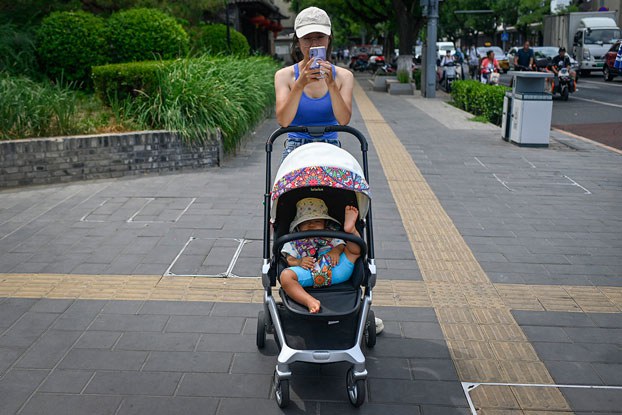 ENG_CHN_WOMENSDAYBirths_03072024.2.jpg A woman pushing a baby carriage waits to cross a street in Beijing, July 10, 2023. (Wang Zhao/AFP)