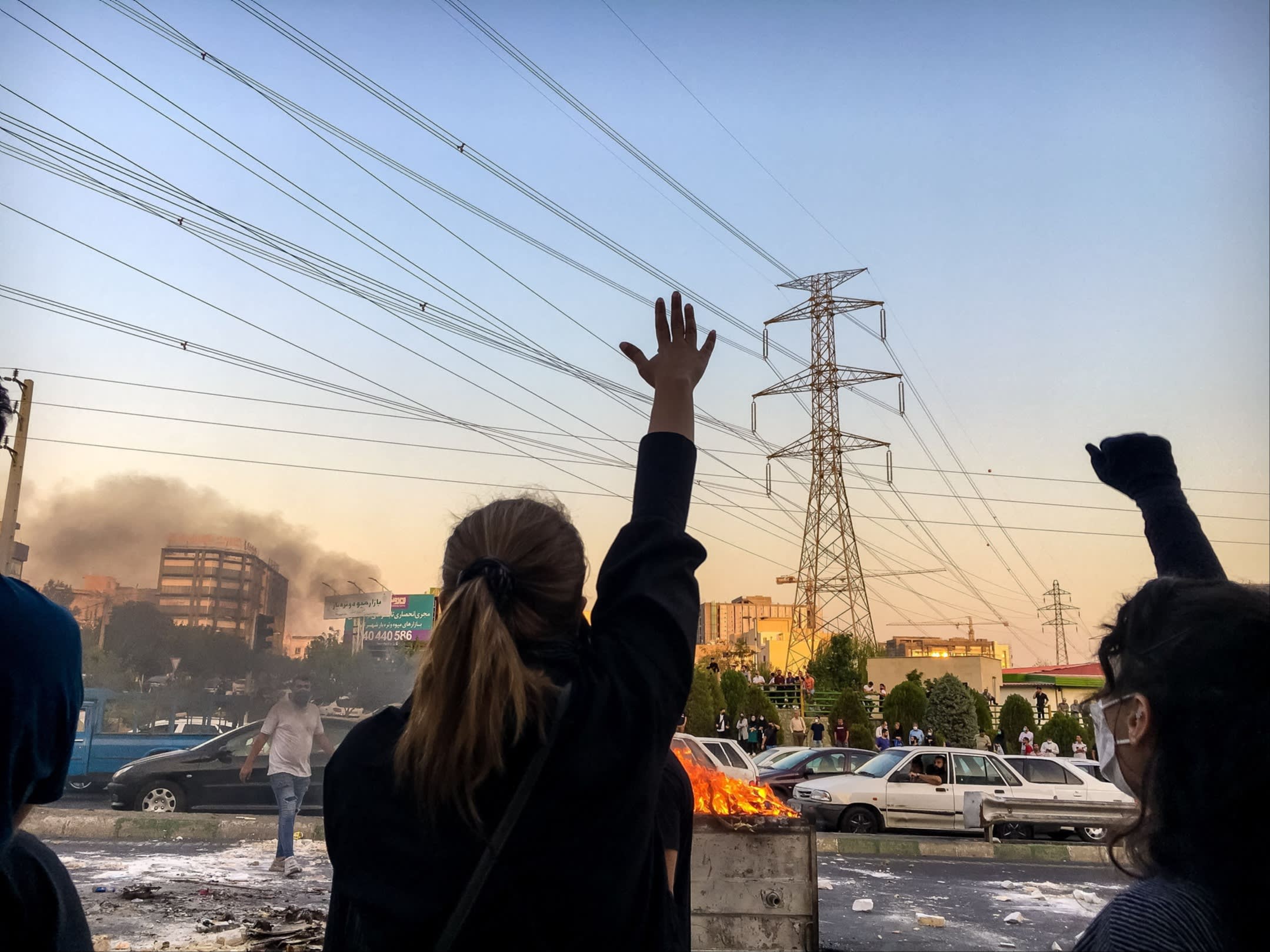 Two women in silhouette, with their backs to the camera, raise their arms to the sky in protest