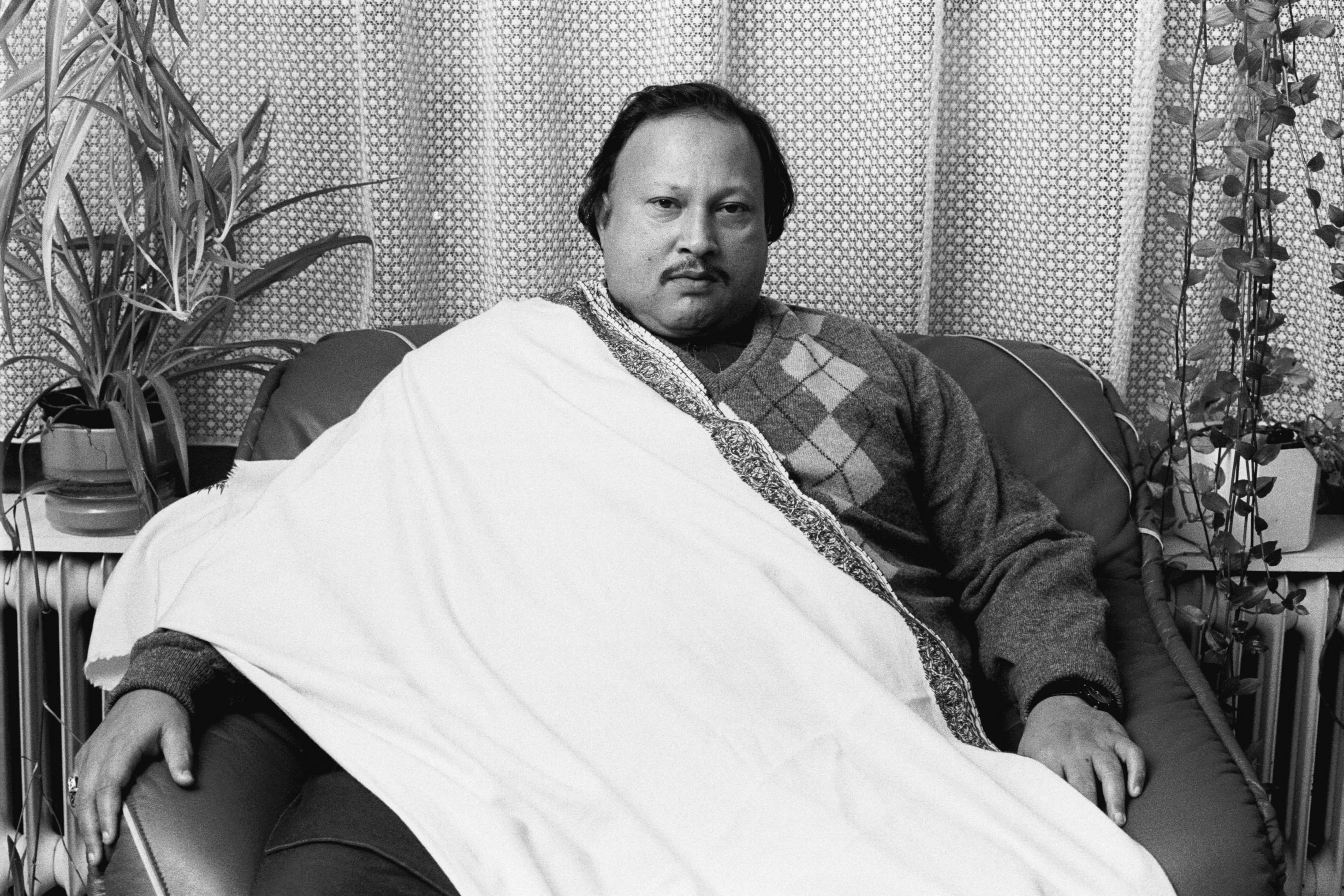 A man sits in an armchair with a white robe draped diagonally across him