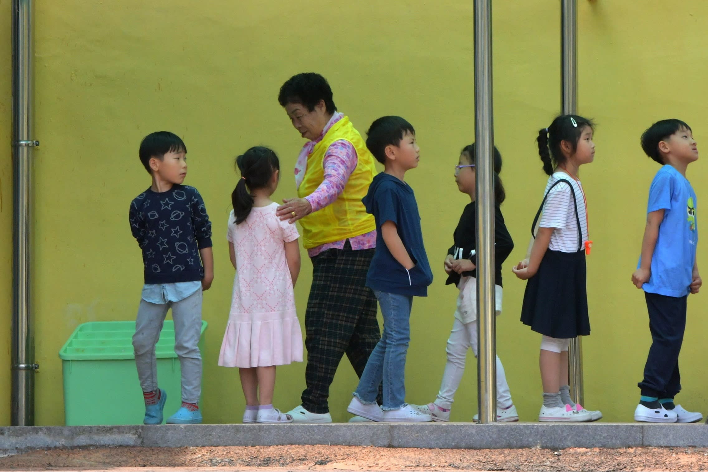 An elderly South Korean woman walks past young students at a school