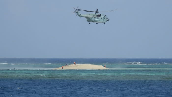 A Chinese helicopter hovers as Filipino scientists inspect the Philippine-held Thitu Island