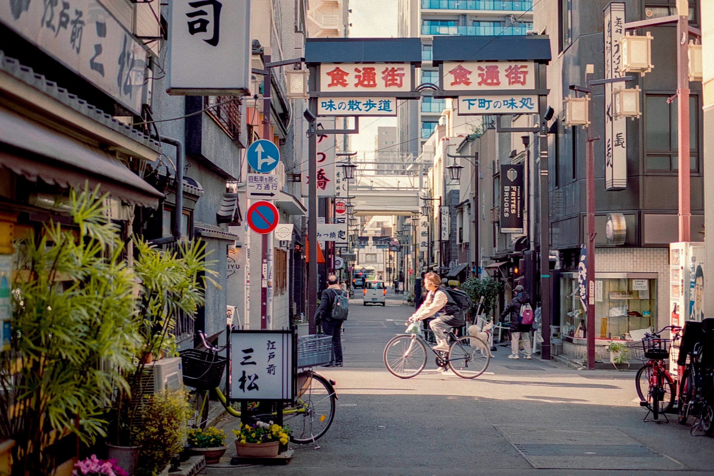 The exterior of Edo-mae Mimatsu, in a narrow Asakusa street across which a female cyclist is riding