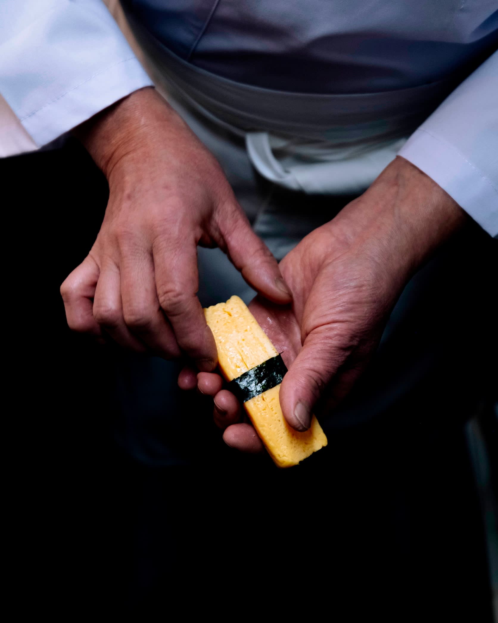 The hands of chef Okuzumi assembling a piece of tamago (egg) nigiri