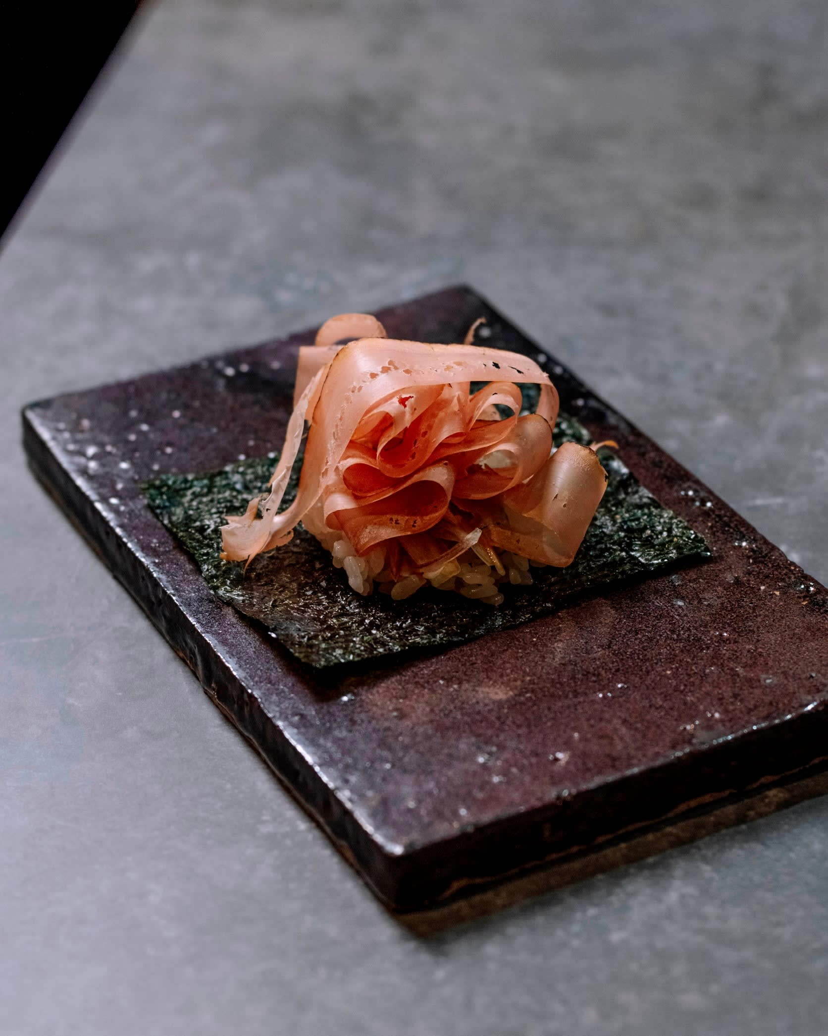 A piece of katsuobushi (bonito flake) temaki sushi on a small rectangular black plate at Sushi Yuko