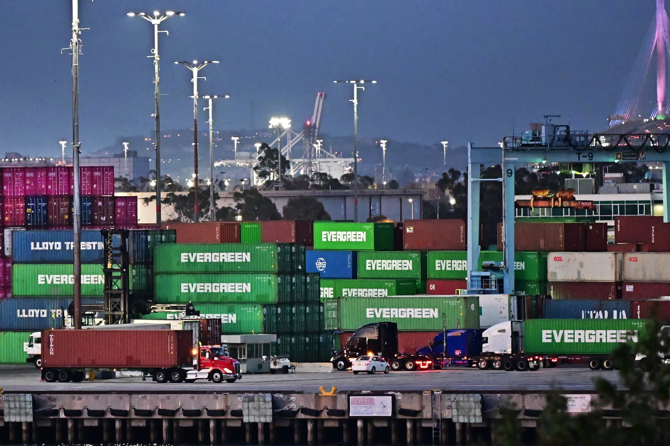 Container trucks make their way past shipping containers stacked high at the Port of Los Angeles on April 14, 2025 in Los Angeles, California.